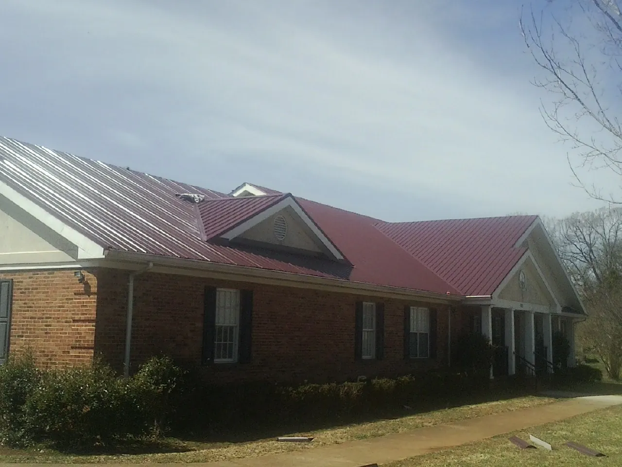 Red metal roof with gabled entries on a long brick building, from a Hail Damage Roof Repair job in Brightwaters