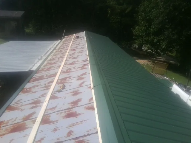 Old rusted panels beside newly installed green metal roofing — Wind Damage Roof Repair by Roofing Brothers in Brightwaters