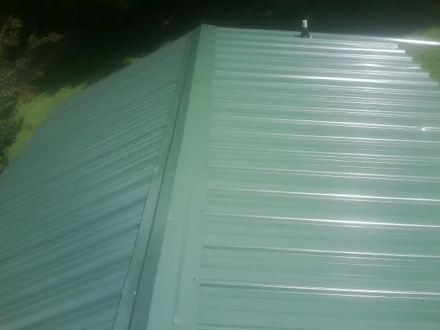 New green metal panels meeting at the ridge of a roof — Flat Roof Repair work by our crew in Brightwaters