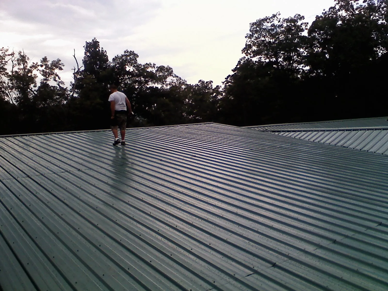 Roofer walking a wide expanse of new green metal roofing in Brightwaters