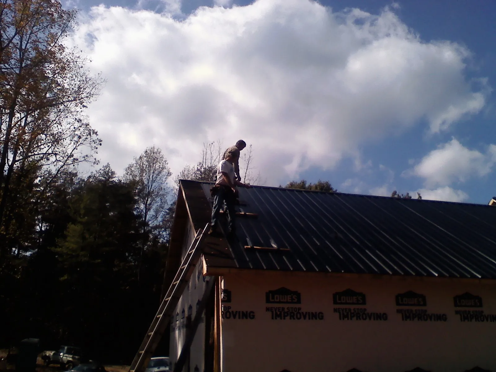 Roofer fastening dark metal panels high against a cloudy sky, from a Roof Inspection job in Brightwaters