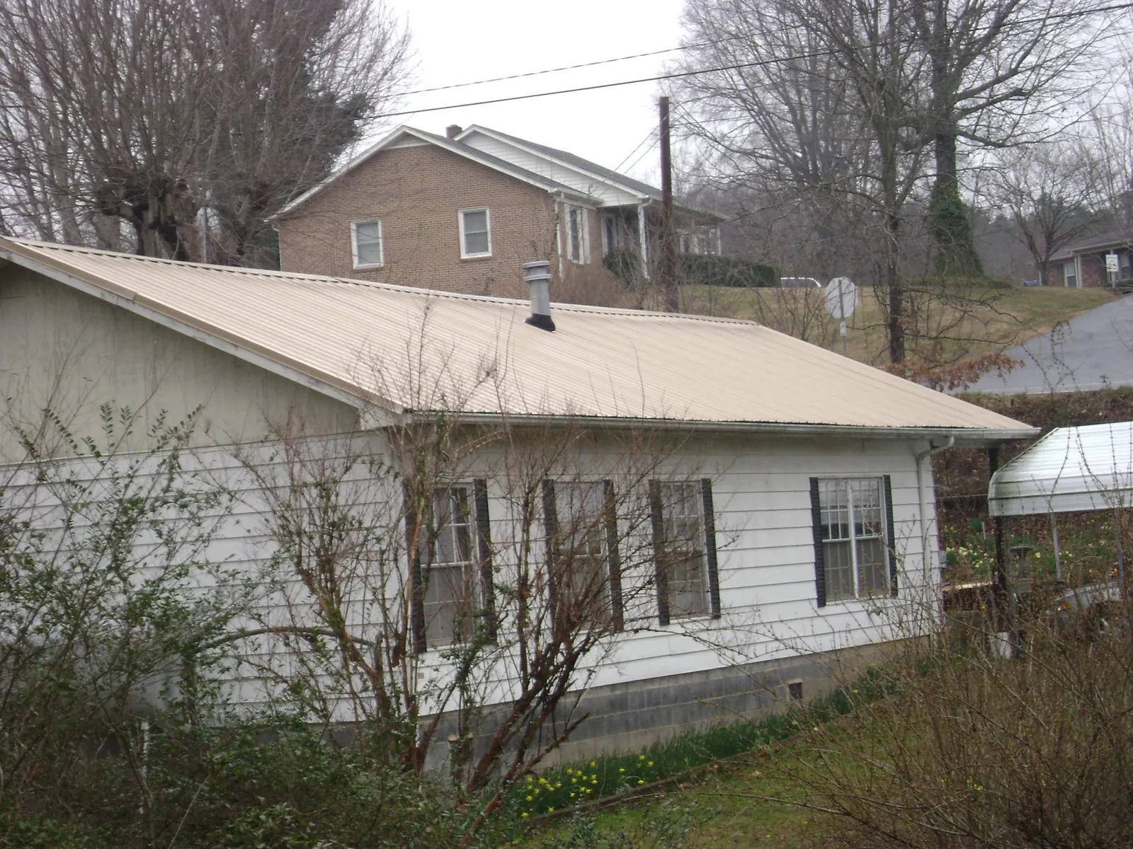 Tan metal roof on a white sided house set into a hillside — Commercial Roofing by Roofing Brothers in Brightwaters