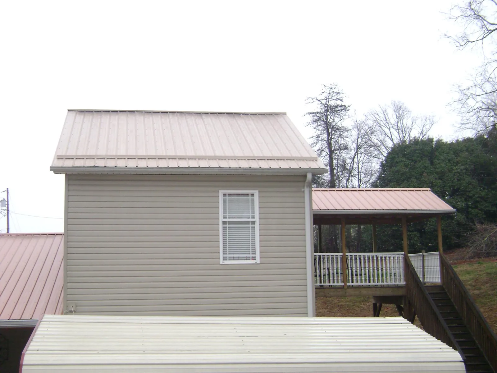 Tan metal roofs on a two story addition and attached porch, from a Roof Replacement job in Brightwaters